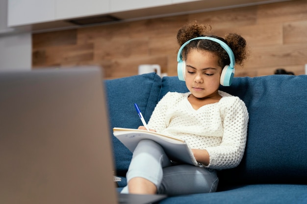 Бесплатное фото Вид спереди маленькой девочки во время онлайн-школы с ноутбуком и наушниками