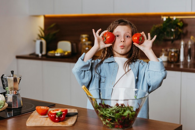 Бесплатное фото Вид спереди маленькой девочки на кухне с овощами