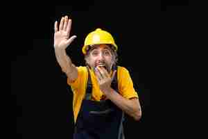 Бесплатное фото Вид спереди мужчины-строителя в желтой форме на черной стене