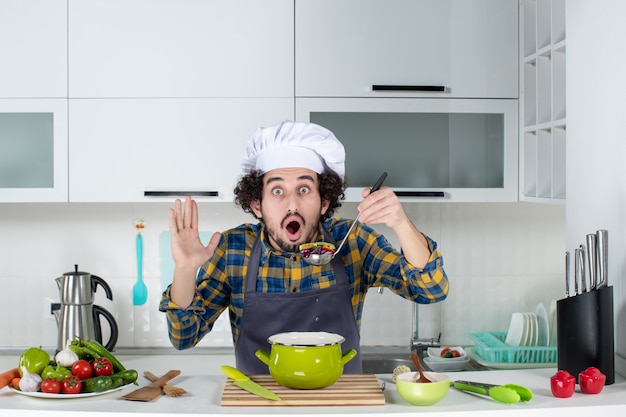 調理済みの食事を味わい、白いキッチンでショックを受けた新鮮な野菜を調理する男性シェフの正面図 無料写真