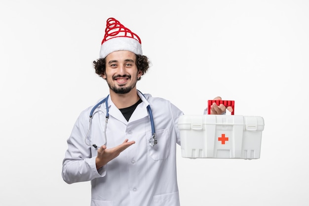 Бесплатное фото Вид спереди мужского врача, держащего аптечку на белой стене