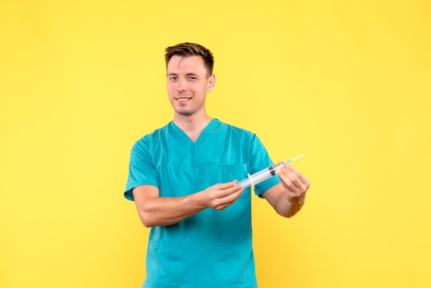 Бесплатное фото Вид спереди мужского врача, держащего огромную инъекцию на желтой стене