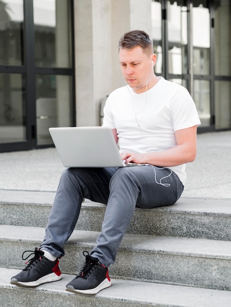 Бесплатное фото Вид спереди человека на открытом воздухе на шагах, работающих на ноутбуке