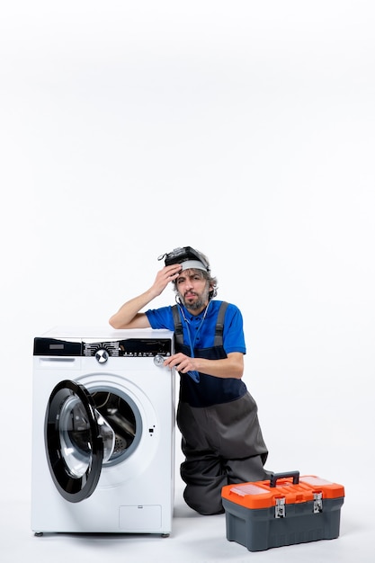 Бесплатное фото Вид спереди размышляющего ремонтника, сидящего рядом с сумкой для инструментов стиральной машины на белой стене