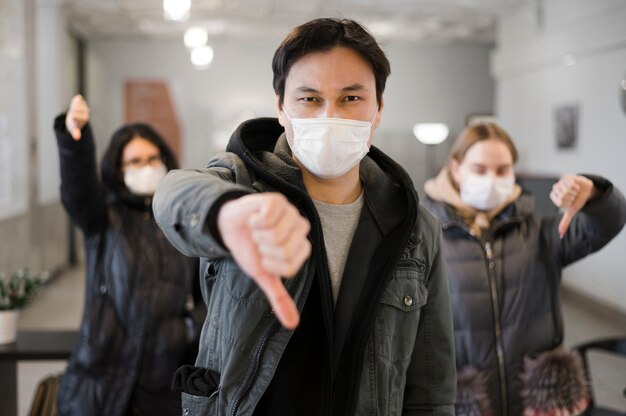 Бесплатное фото Вид спереди людей, носящих медицинские маски и дает большие пальцы вниз