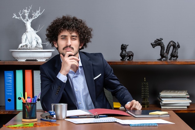Бесплатное фото Вид спереди серьезного бизнесмена, сидящего за столом в офисе