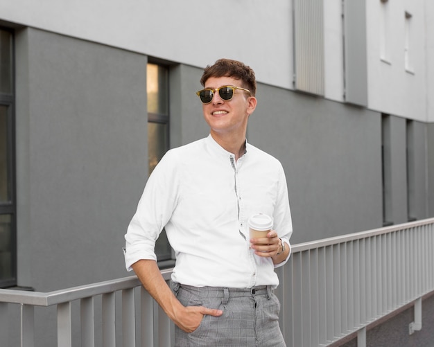 Бесплатное фото Вид спереди стильного человека в солнцезащитных очках, держащего чашку кофе на открытом воздухе