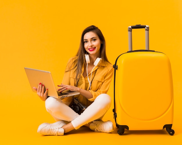 Бесплатное фото Вид спереди женщина держит ноутбук и позирует рядом с багажом