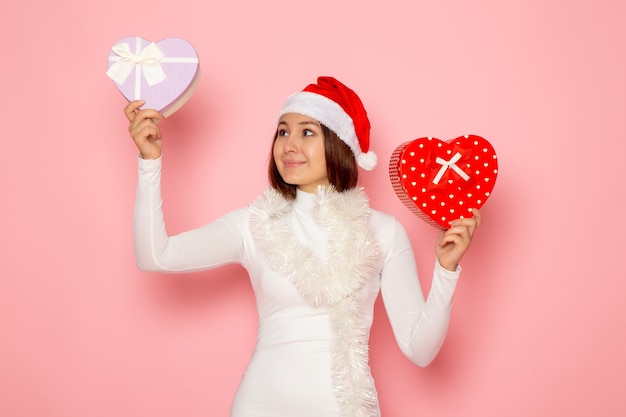 無料写真 ピンクの壁にハート型のプレゼントを保持している赤い帽子の若い女性の正面図