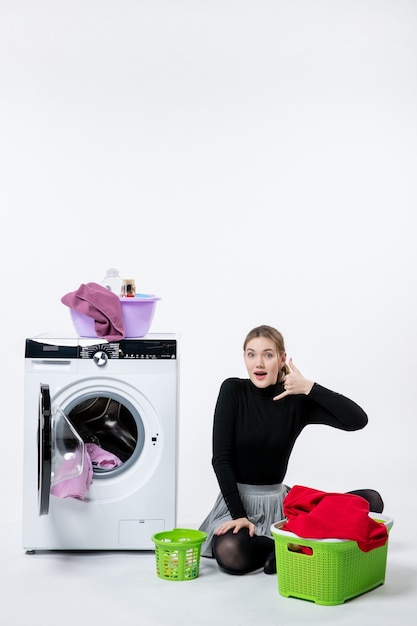 Бесплатное фото Вид спереди молодой женщины со стиральной машиной, складывающей грязную одежду на белой стене