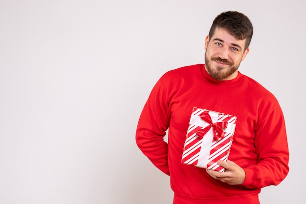 Бесплатное фото Вид спереди молодого человека в красной рубашке, держащего рождественский подарок на белой стене