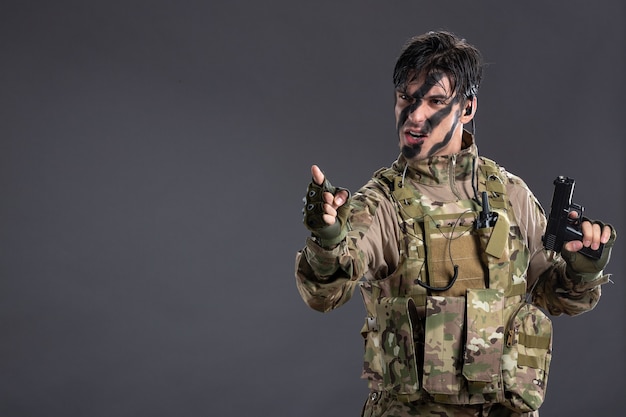 무료 사진 어두운 벽에 총을 든 위장을 한 젊은 군인의 전면 모습