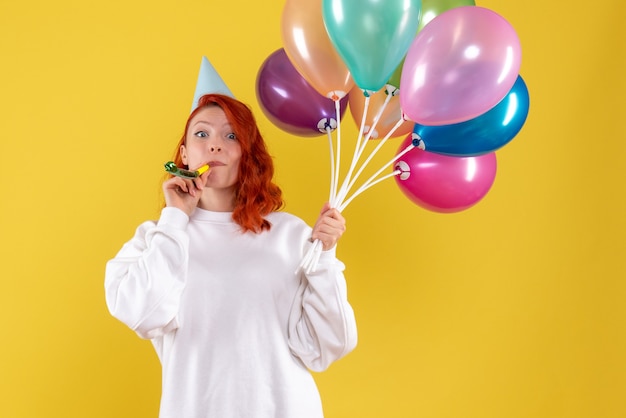 Бесплатное фото Вид спереди молодой женщины, держащей разноцветные шары на желтой стене