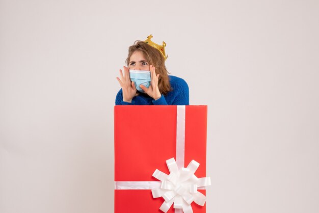 Бесплатное фото Вид спереди молодой женщины внутри подарочной коробки в маске, вызывающей кого-то на белой стене