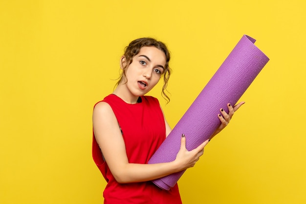 Бесплатное фото Вид спереди молодой женщины с фиолетовым ковром на желтой стене