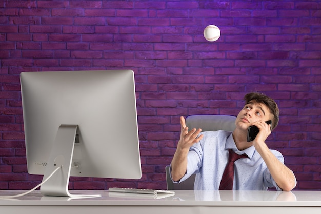 Front view office worker behind office desk holding baseball ball and talking at phone