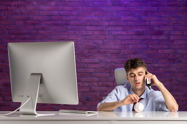 Front view office worker behind office desk holding baseball ball and talking at phone