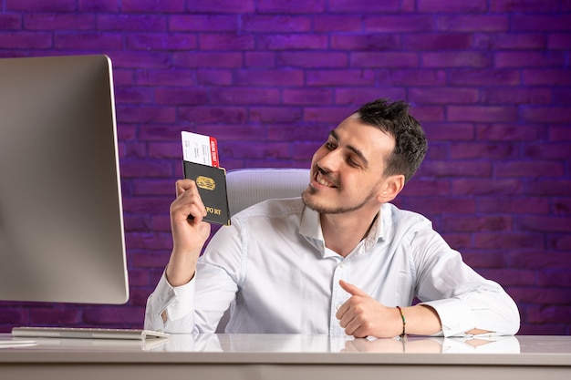 Free photo front view office worker sitting behind his working place holding tickets and passport