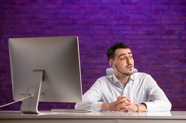 Front view office worker sitting behind his working place and talking through earphones