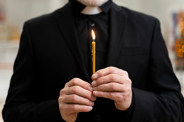 Foto gratuita vecchia candela della holding del sacerdote di vista frontale