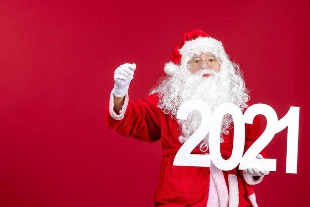 Front view of old santa claus holding writing on red wall