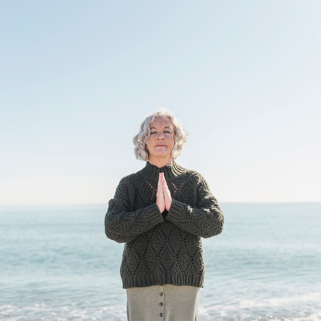 Front view old woman meditating on the beach