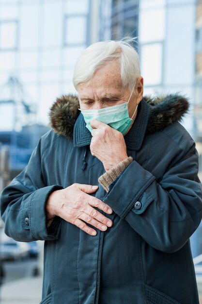 Front view of olden woman in the city wearing medical mask and feeling ill