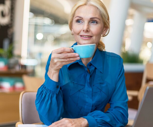 Front view of older business woman enjoying cup of coffee while working