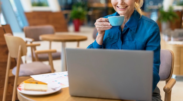 Front view of older business woman having cup of coffee and working on laptop