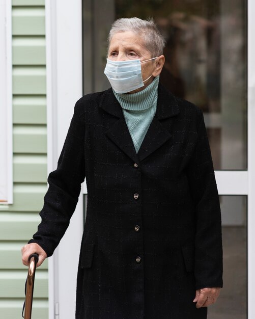 Front view of older woman with medical mask and cane