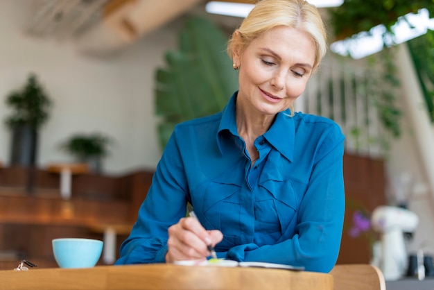 Vista frontale della donna anziana al lavoro con penna e taccuino