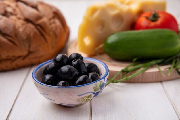 Front view olives with cheese  tomato  cucumber on a stand  with a loaf of black bread on a white background