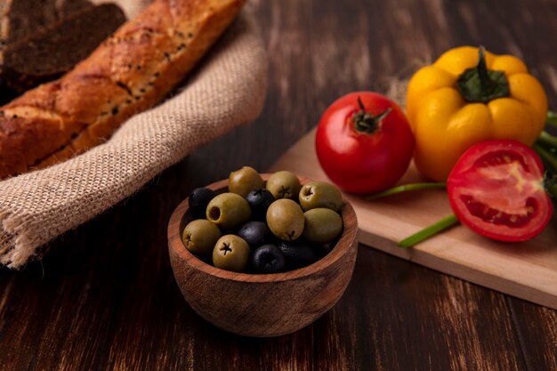 Front view olives with tomatoes  bell peppers on a board and a loaf of bread on a wooden background