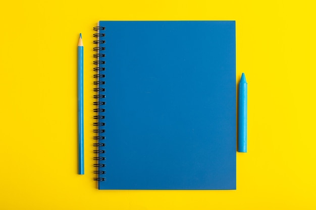 Quaderno blu aperto vista frontale con matita sullo scrittorio giallo