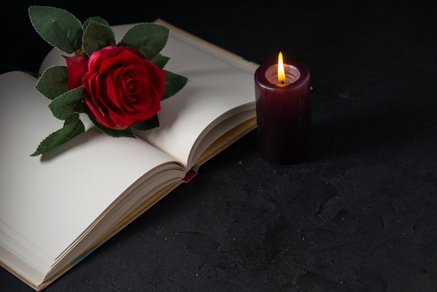 Front view of open book with candle and red flower on black