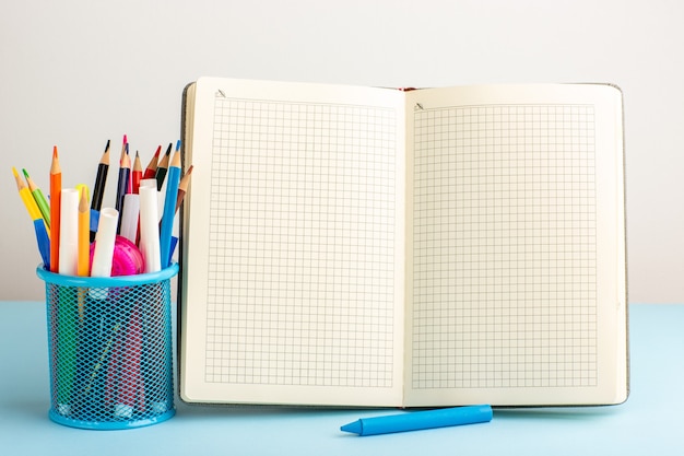 Front view open copybook with felt pens and pencils on blue desk