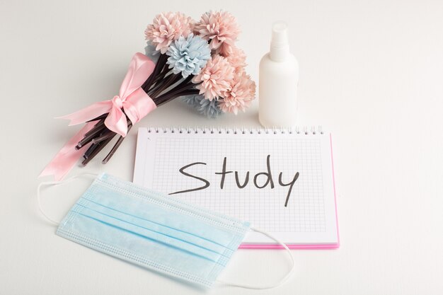 Front view open copybook with spray mask and flowers on white surface