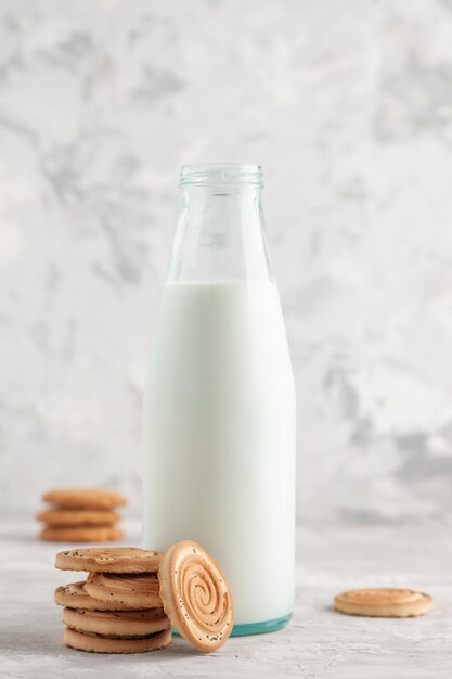 Front view of an open glass bottle filled with milk and cookies on stained white background with free space