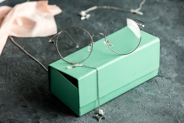 A front view optical sunglasses on the turquoise sunglasses box and grey desk with silver bracelets isolated sight vision eyes