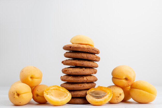 A front view orange apricots whole and  flavored with cookies on the light desk 