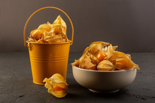 A front view orange fruits inside peels and yellow bucket isolated on dark