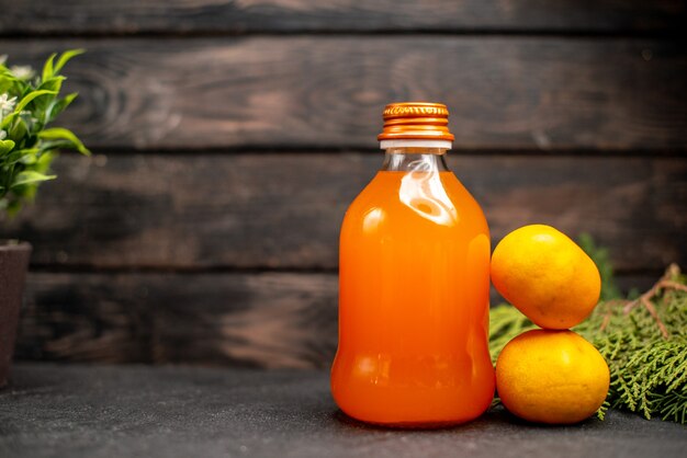 Front view orange juice in bottle fresh oranges pine tree branches on brown isolated surface