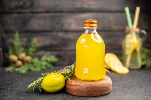 Front view orange juice in bottle on wood board lemon on dark wooden surface