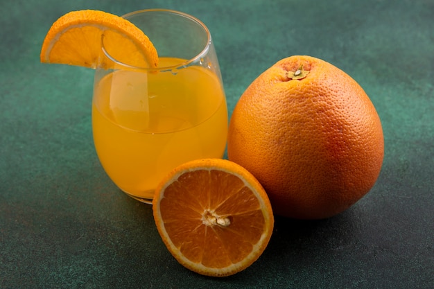 Free photo front view orange juice in glass with orange and grapefruit on green background