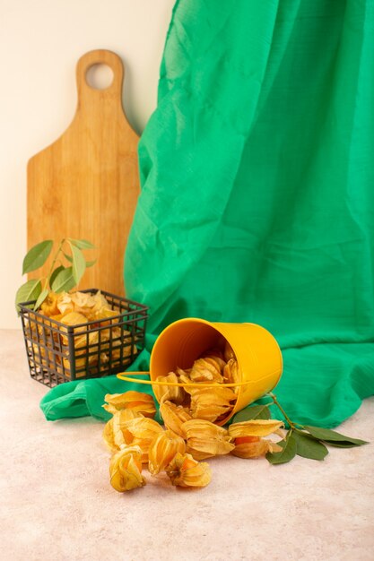 A front view orange peeled physalises inside bucket with green tissue on the pink desk  