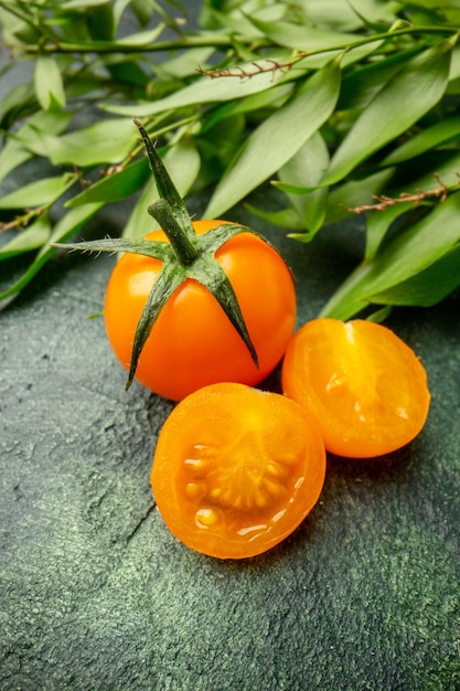 짙은 녹색 표면에 녹색 잎이 있는 전면 보기 오렌지 토마토