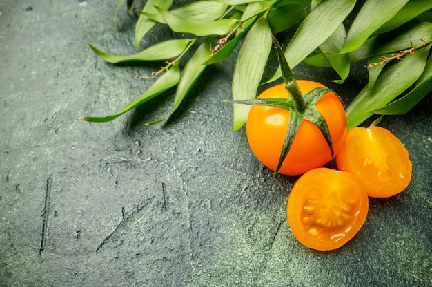 Front view orange tomatoes with green leaves on dark green surface