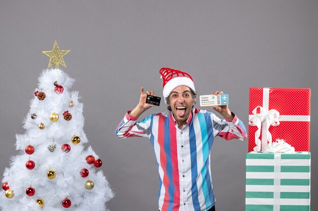 Front view overjoyed man showing his tongue holding card and travel ticket