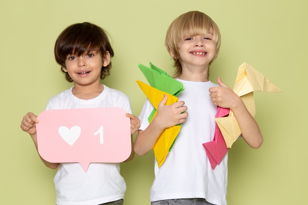 A front view pair of boys smiling adorable sweet cute happy holding paper figures on the stone colored space