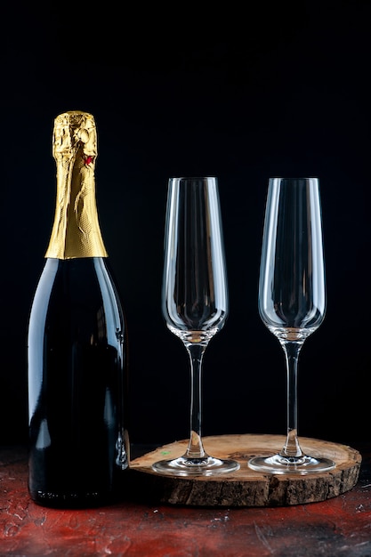 Вид спереди пара бокалов для шампанского на деревянной доске и бутылка шампанского